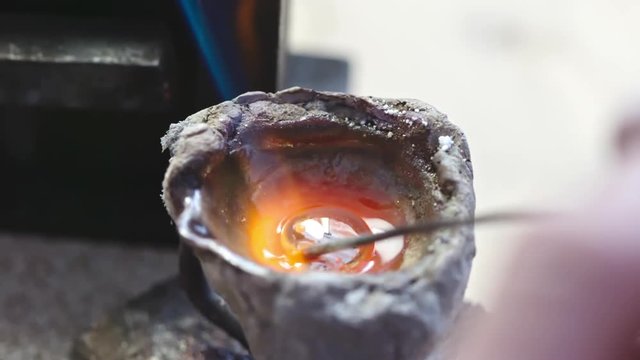 Zoom in of liquid precious metal melting in bowl with gas torch for making new jewelry