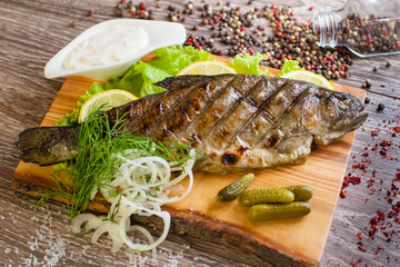 Grilled trout on a wooden board with lemon, pickles and sauce. d