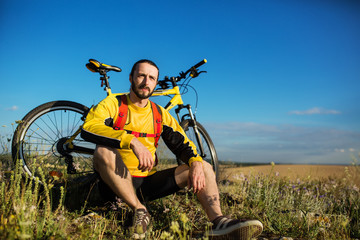 Cyclist resting on grass in mountains. Man is looking aside.