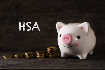 HSA" words Piggy bank and stack of golden money increased with wooden background - saving, finance and business concept