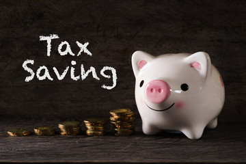 "Tax saving" words with Piggy bank and stack of golden money increased with wooden background - saving, finance and business concept