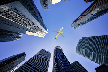 Obraz premium Wysokie budynki miasta i samolot lecący nad głową