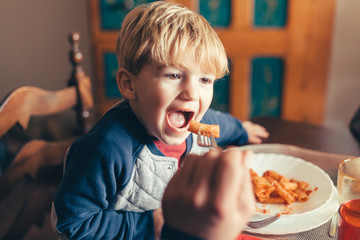 Blond child eats tomato pasta dish for lunch with family on Christmas Day