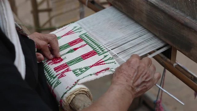 Old woman weaving white red and green cotton flag pattern on loom
