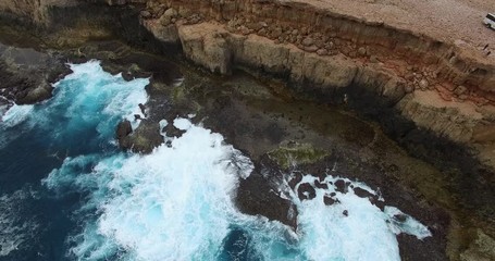 Vertical ascent in drone from low level aerial flight of big swells breaking againt a rugged cliffs at Shark Bay in Western Australia