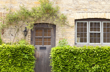 Fototapeta na wymiar Brown rustic wooden doors in an old traditional English stone honey colored cottage, green hedge in front