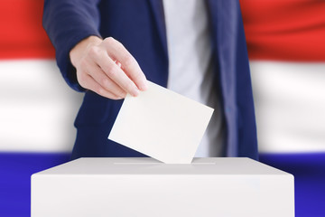 Voting. Man putting a ballot into a voting box with Holland flag on background.
