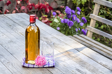 Bottle whiskey and glass with flower on table in garden
