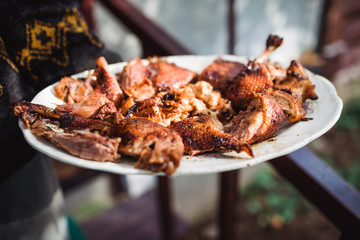 man's hand holds grilled roast chicken on white plate