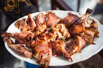 man's hand holds grilled roast chicken on white plate