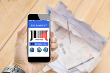 man holding smart phone online bill payment with bar code scan with blurred utilities bill on...
