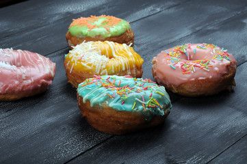 Fresh tasty donuts in soft colorful glaze on a black and white wooden background