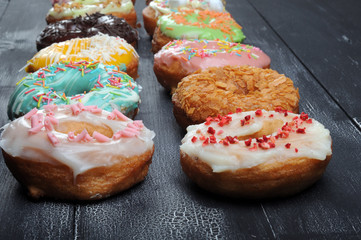 Fresh tasty donuts in soft colorful glaze on a black and white wooden background