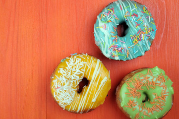 Fresh tasty donuts in soft colorful glaze on a orange wooden background