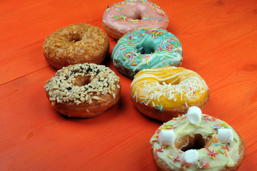 Fresh tasty donuts in soft colorful glaze on a orange wooden background