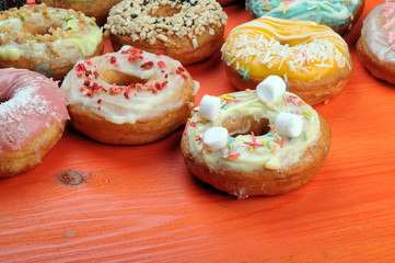 Fresh tasty donuts in soft colorful glaze on a orange wooden background