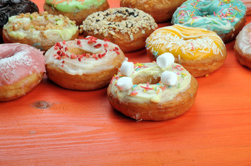 Fresh tasty donuts in soft colorful glaze on a orange wooden background