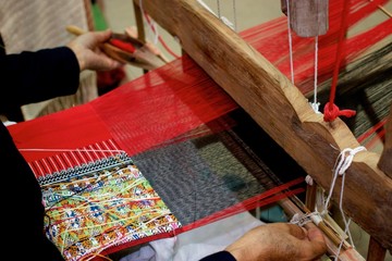 Old woman weaving red black and multi color cotton flag pattern on loom in North of Thailand