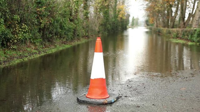 Floods after storm, heavy rain, traffic cone warning on flooded road