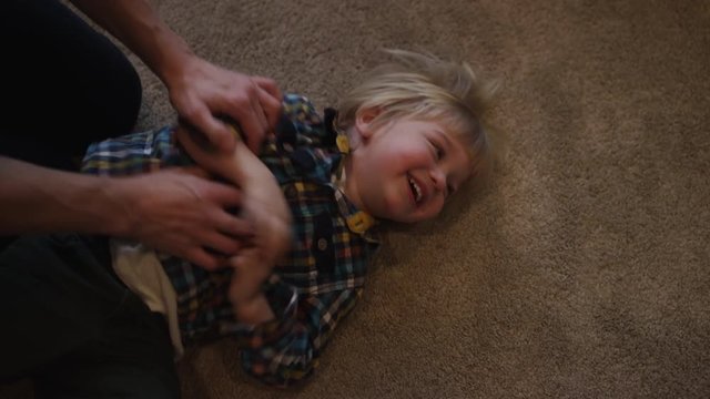 A young boy is tickled while rolling around on a carpeted floor.