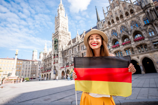 Portrait of a young female tourist with german flag standing on the central square in front of the town hall building in Munich. Having a great vacation in Germany