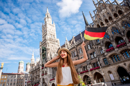 Portrait of a young female tourist with german flag standing on the central square in front of the town hall building in Munich. Having a great vacation in Germany