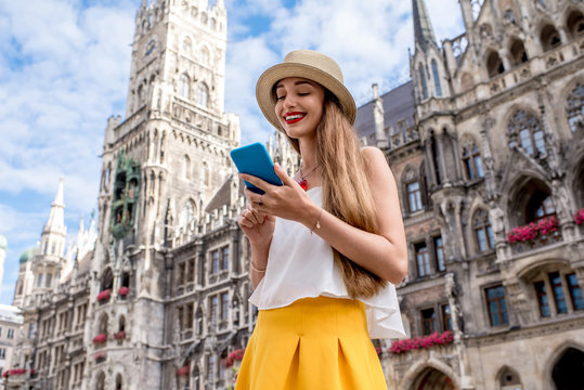 Young female tourist using mobile phone on the central square in front of the famous town hall building in Munich