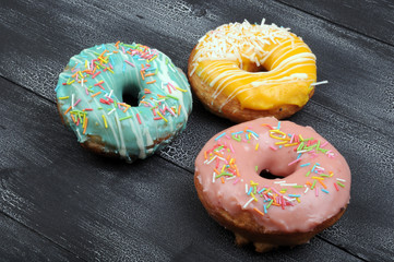 Fresh tasty donuts in soft colorful glaze on a black and white grunge  wooden background