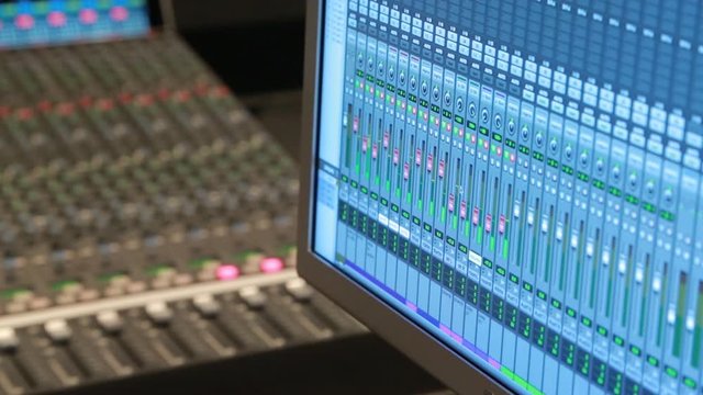 Close up of a digital audio workstation with an audio console in the background in a music studio.