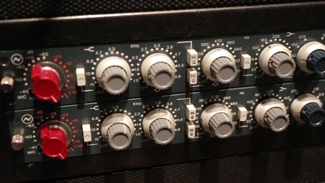 Steadicam close up shot of knobs on an audio compressor in a music studio.