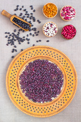 Beans of different colors in a wicker plate and bowls on sacking