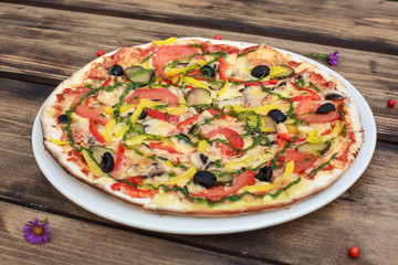 Vegetable pizza served on white plate on wooden table 

