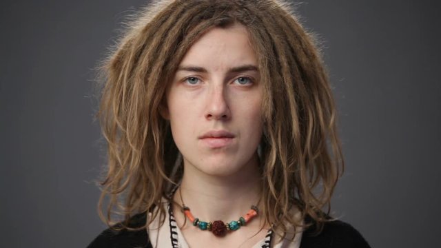 Close up young woman with dreadlocks looking straight, gray background
