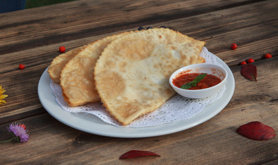 Chibureks (meat patties) on wooden table with tomato sauce
