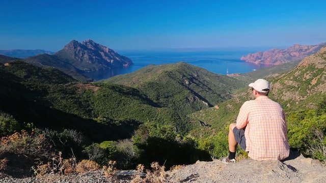 Young attractive man enjoying the view from famous D81 coastal road with view of Golfe de Girolata from Bocca Di Palmarella, Corsica, France, Europe