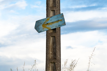 Gelber Pfeil auf blauem Grund an Steinmast am Jakobsweg in Spanien