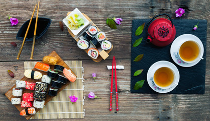A variety of sushi and green tea set on rustic wooden table.