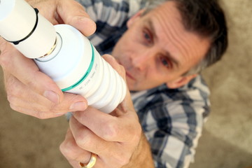Man fitting a low energy CFL light bulb to replace an old-fashio