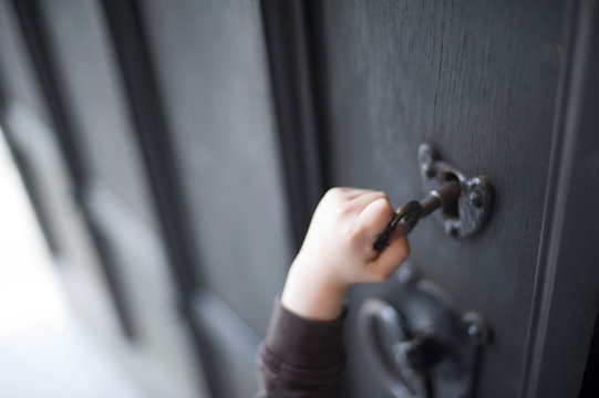 Child reaching up to unlock an old wooden door