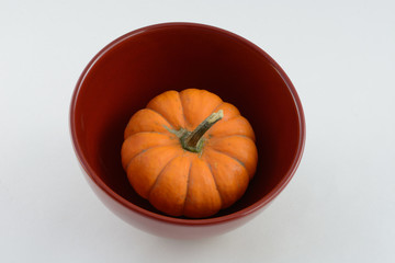 Small raw pumpkin in red bowl against white background