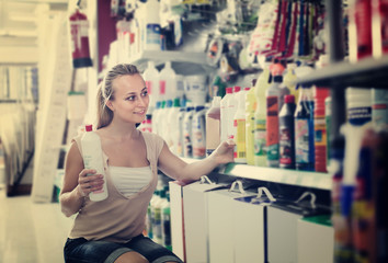 happy young woman customer choosing paint medium in bottle in hy