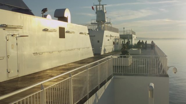 Sunny ferry deck with people, ocean, mountains, and mist.