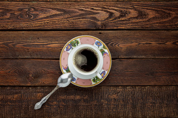 Coffee cup on dark wood table with plate and spoon. Top view
