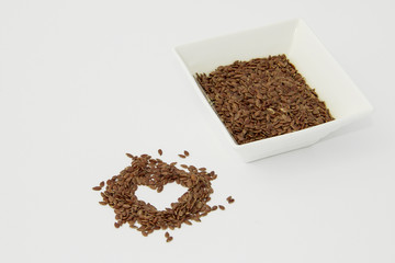Flax seed in a ceramic container isolated on a white background. Flax seed in the shape of an heart.