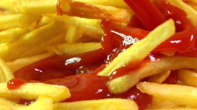 Adding tomato ketchup to french fries. Popular fast food, deep fried potato chips. Super slow motion macro video