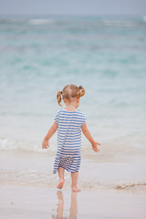 Fototapeta na wymiar Toddler girl in striped dress goes to the ocean. Summer vacations. Freedom