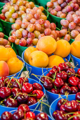 Fresh cherries, apricots and red grapes in pots on display at farmers market