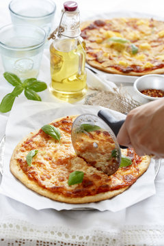 Close-up of human hand cutting pizza margherita