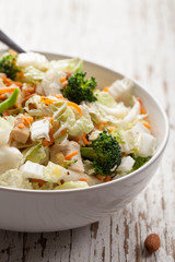 Side view of an Asian Napa cabbage salad with organic broccoli, almonds, chicken, and a rice vinaigrette on weathered white wood