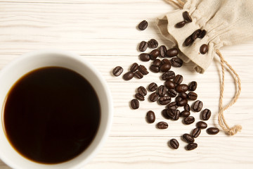 Cup of coffee and coffee beans in a fabric bag on the wood backg